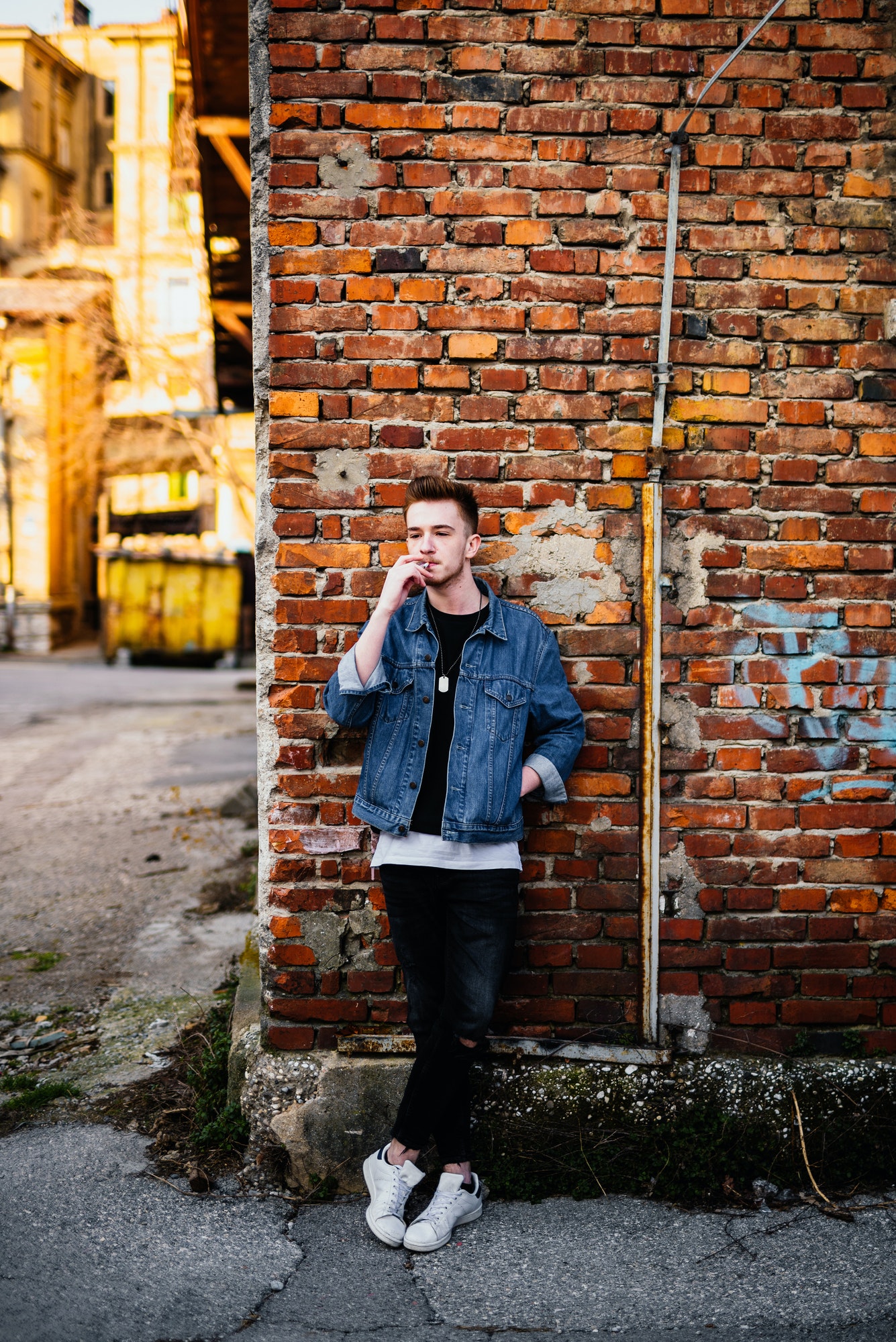 Young man in front of brick wall smoking cigarette